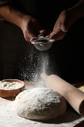 Man sprinkling flour over dough at wooden table, closeup