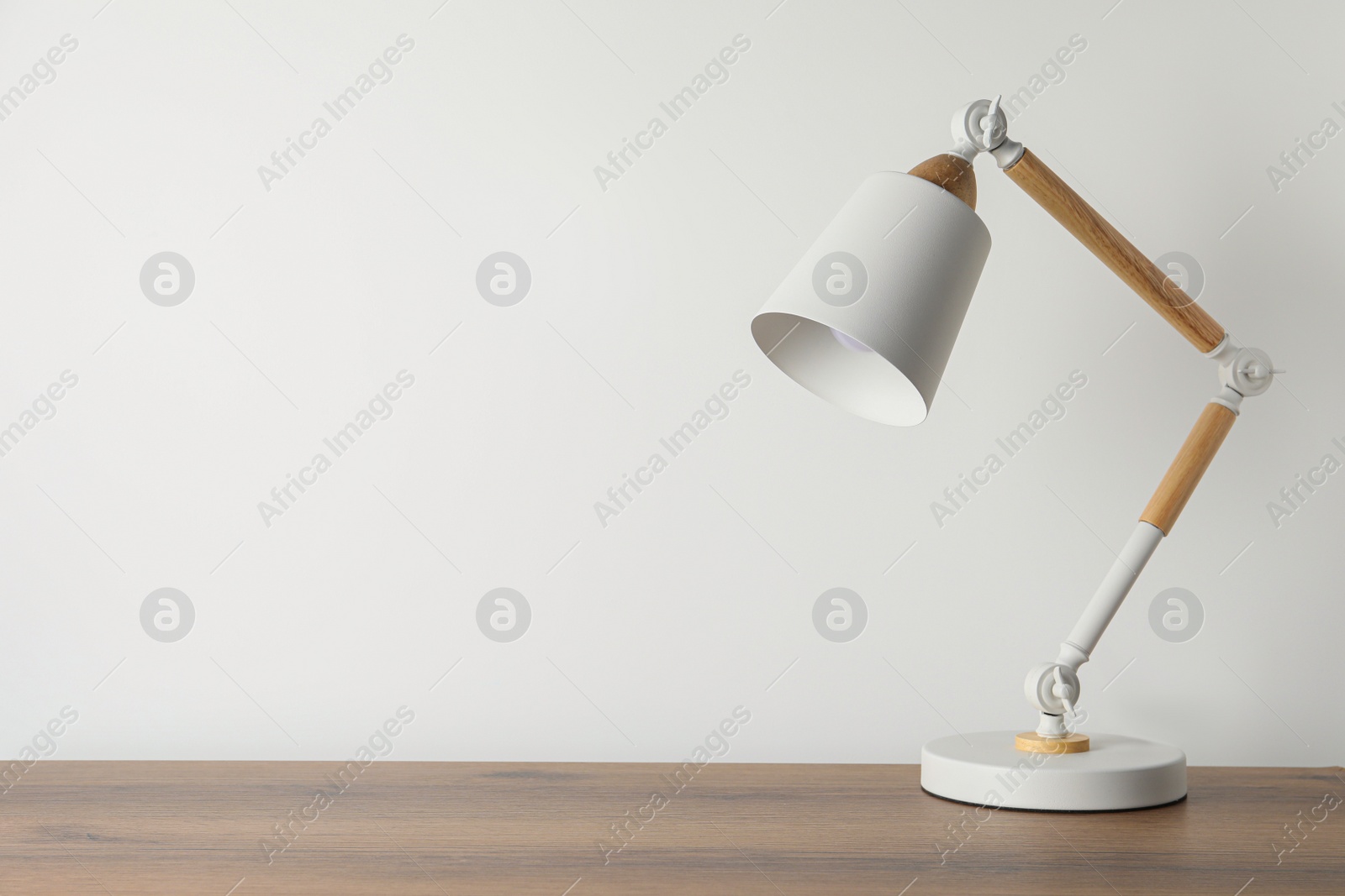Stylish modern desk lamp on wooden table near white wall, space for text Photo of Stylish modern desk lamp on wooden table near white wall, space for text