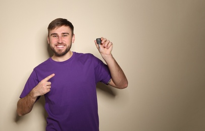 Photo of Happy young man with car key on color background, space for text. Getting driving license