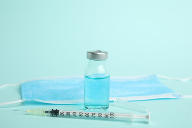 Photo of Vial, syringe and surgical mask on turquoise background. Vaccination and immunization