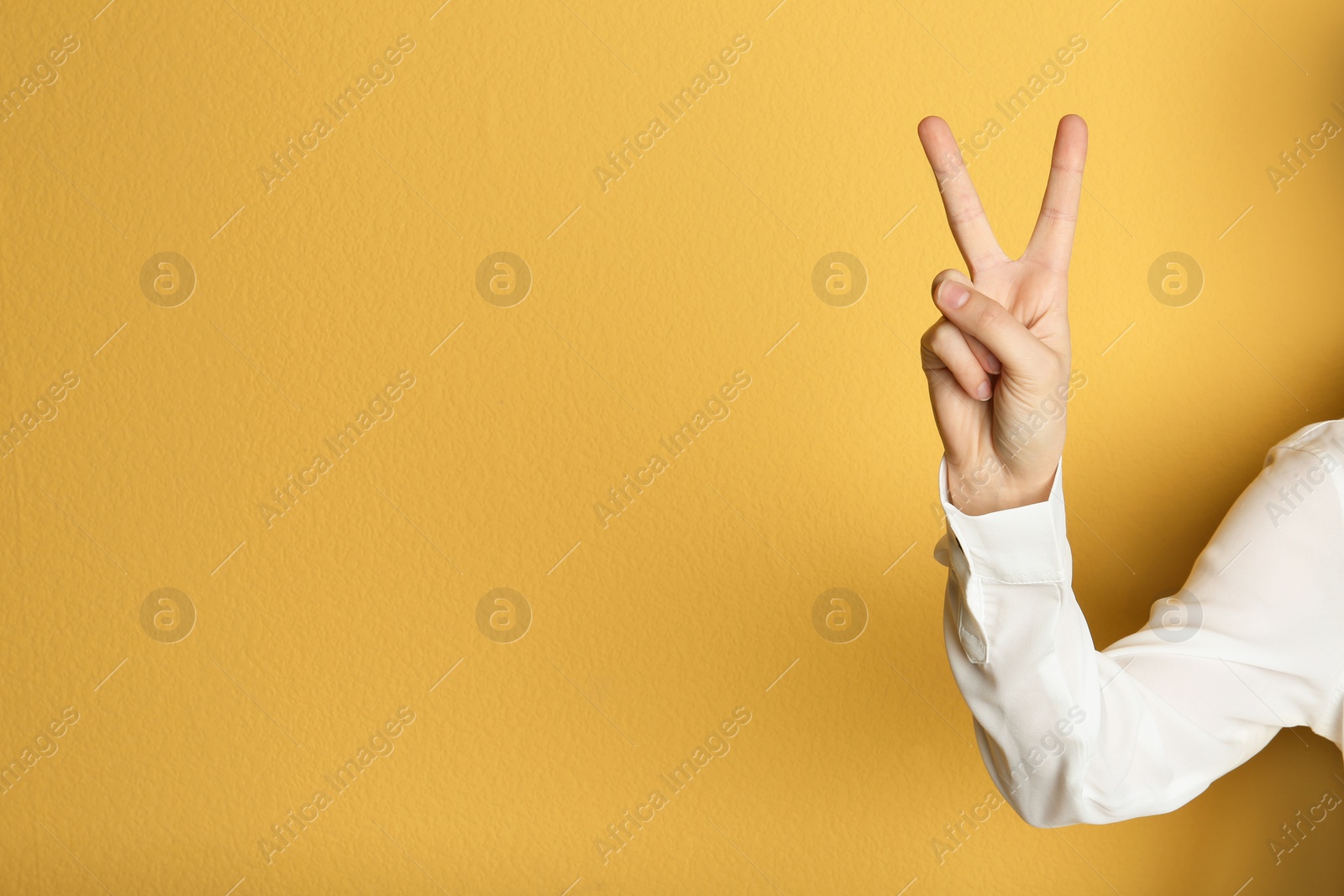 Photo of Young woman showing victory gesture on color background. Space for text