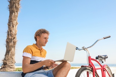 Photo of Attractive man with laptop and bike outdoors on sunny day