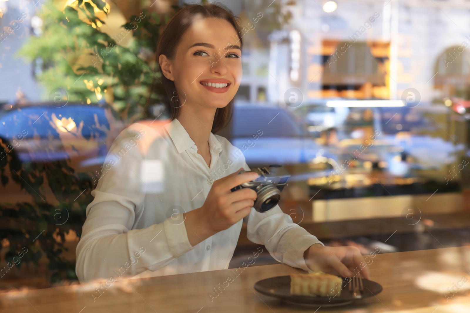 Photo of Young woman taking photo of plate with pie at cafe, view through window. Creative hobby