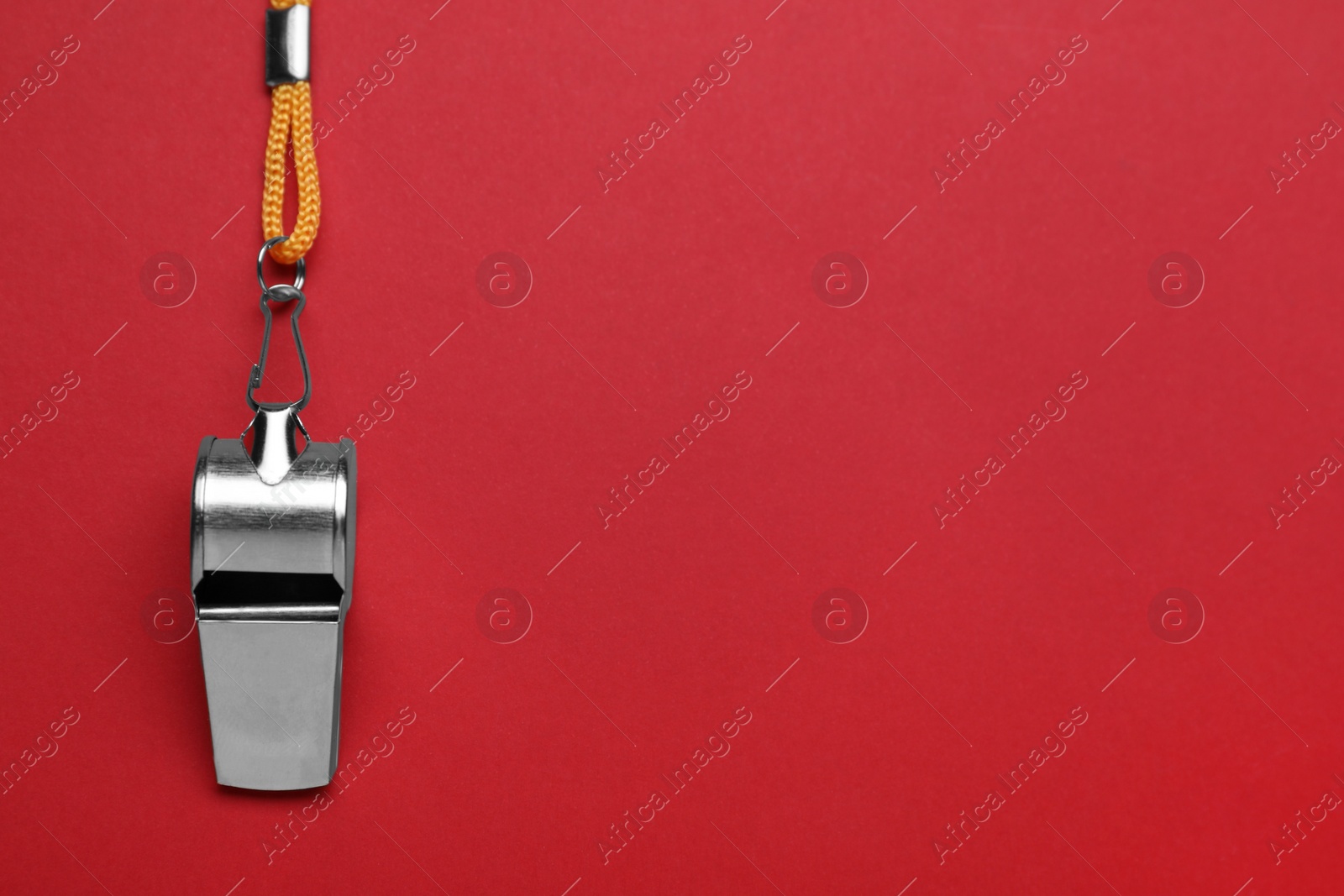 Photo of One metal whistle with cord on red background, top view. Space for text