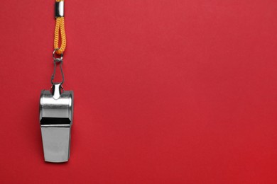 Photo of One metal whistle with cord on red background, top view. Space for text