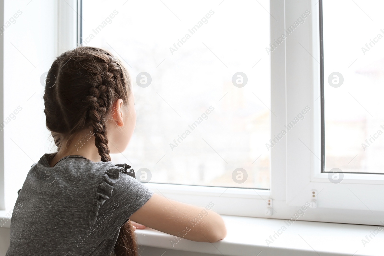 Photo of Lonely little girl near window indoors. Child autism