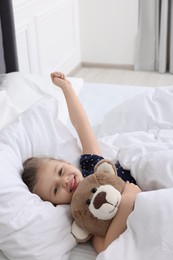 Photo of Cute little girl lying with teddy bear in bed at home
