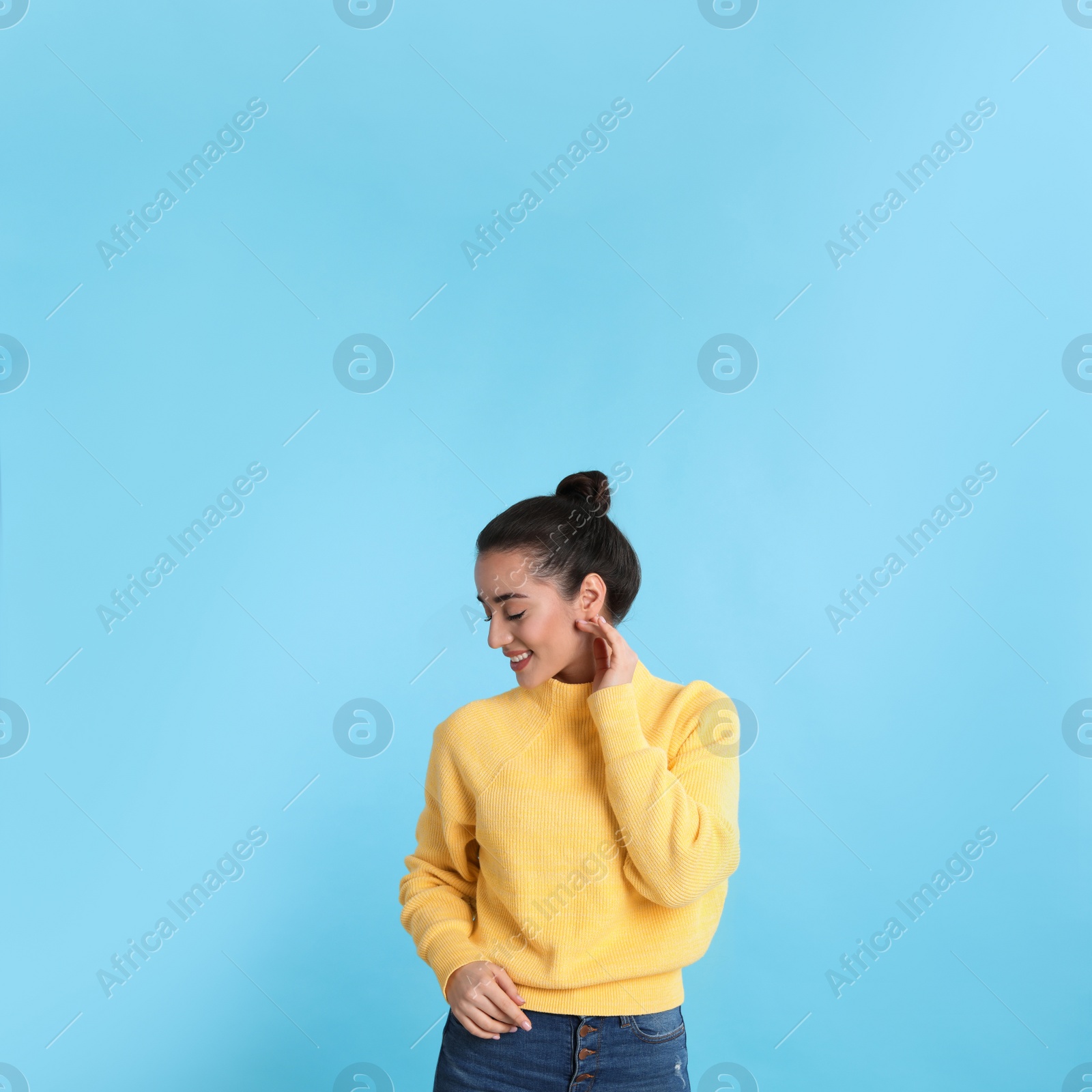 Photo of Beautiful young woman wearing yellow warm sweater on light blue background. Space for text