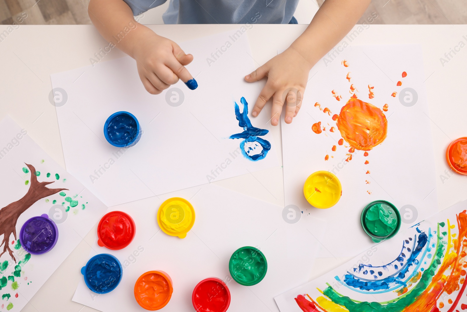 Photo of Little child painting with finger at white table indoors, top view