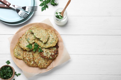 Delicious zucchini fritters served on white wooden table, flat lay. Space for text