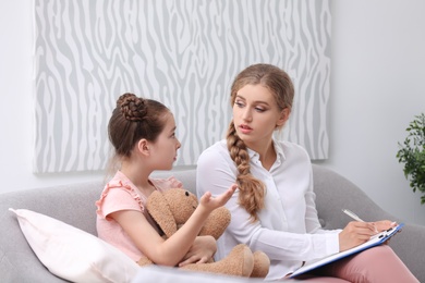 Photo of Young female psychologist working with little child in office