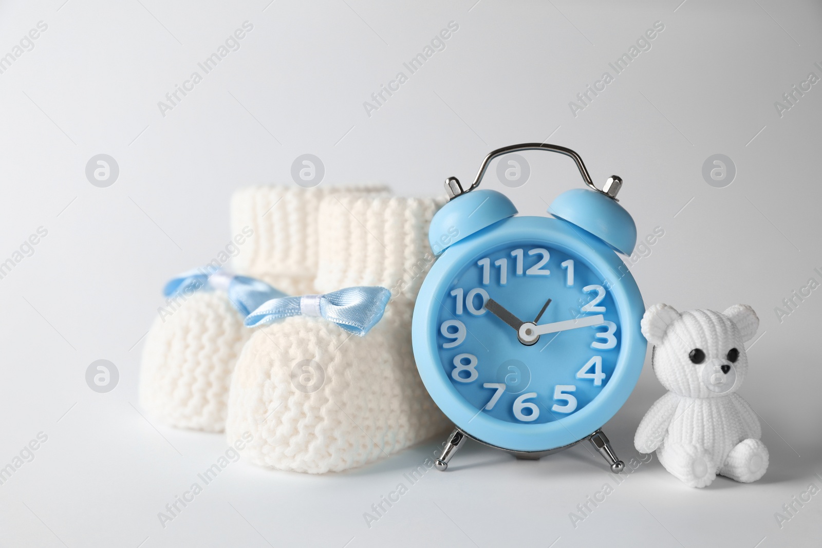 Photo of Alarm clock, toy bear and baby booties on white background. Time to give birth