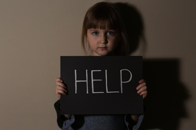 Abused little girl with sign HELP near beige wall. Domestic violence concept