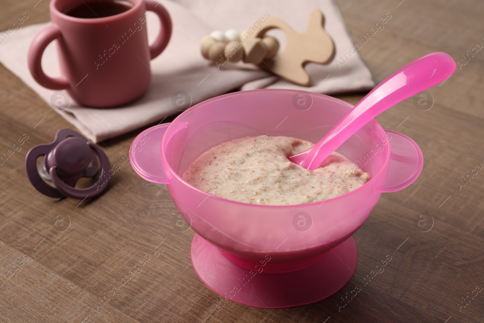 Photo of Baby food. Puree in bowl, drink, toy and soother on wooden table