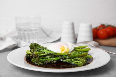 Photo of Tasty cooked broccolini with poached egg and sauce on grey table, closeup