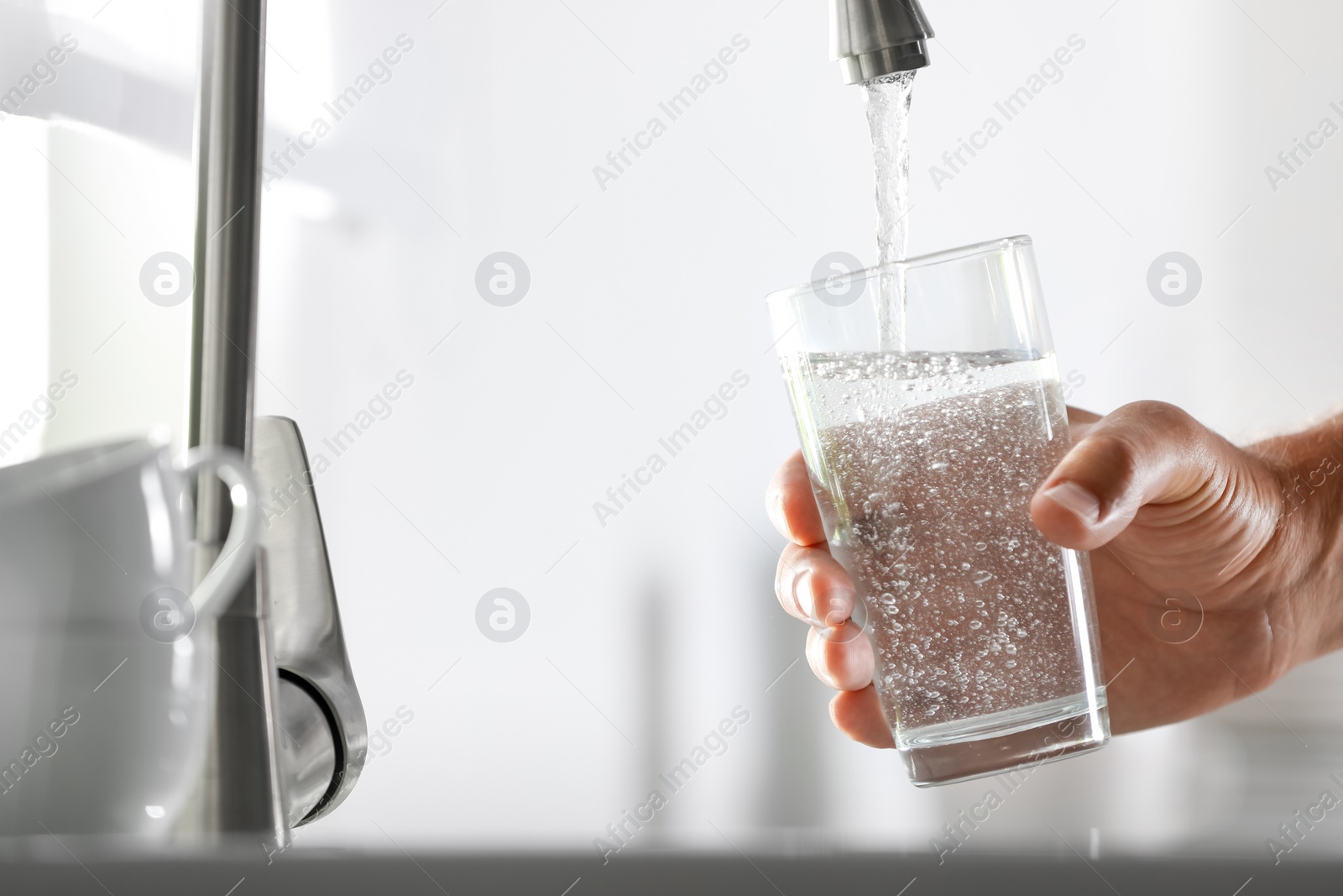 Photo of Man pouring water into glass in kitchen, closeup