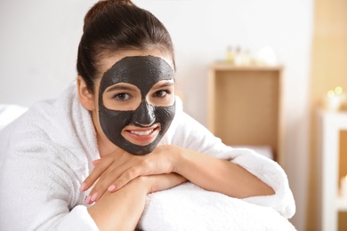 Beautiful woman with black mask on face relaxing in spa salon. Space for text