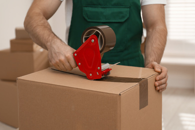 Man packing box with adhesive tape indoors, closeup. Moving service