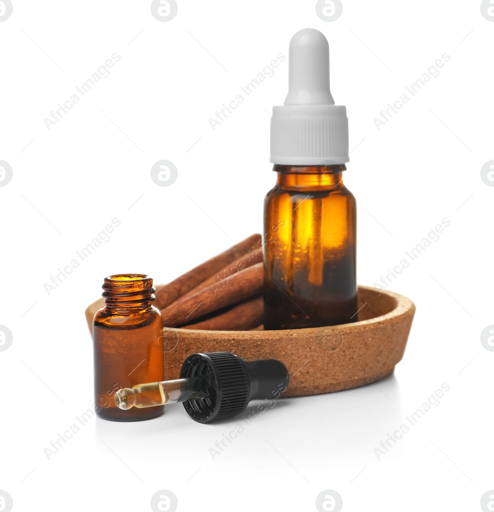 Photo of Bottles of cinnamon oil, dropper and sticks on white background