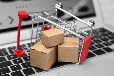 Internet store. Small cardboard boxes and shopping cart on laptop, closeup