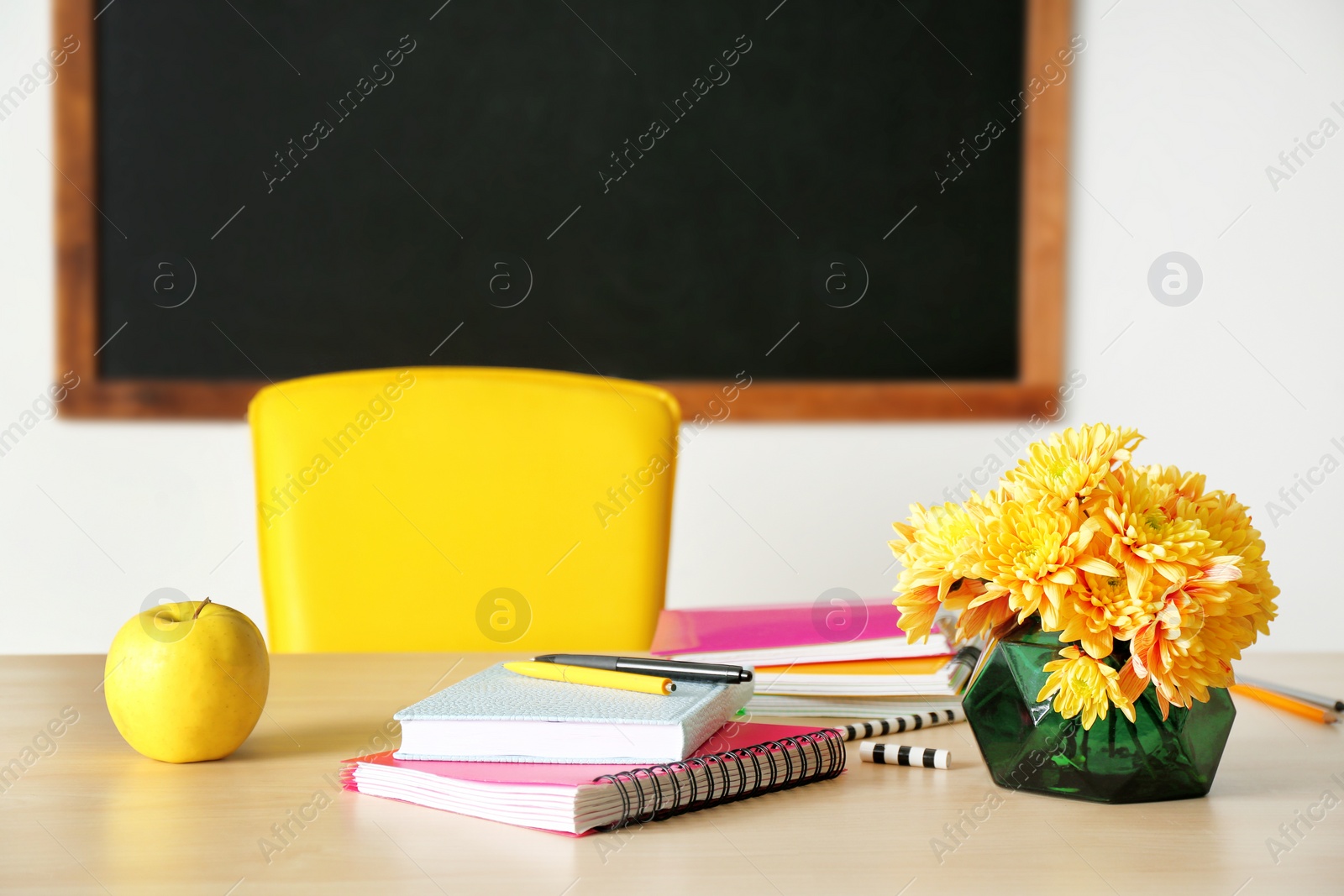 Photo of Bouquet of flowers, apple and notebooks on table in classroom. Teacher day celebration