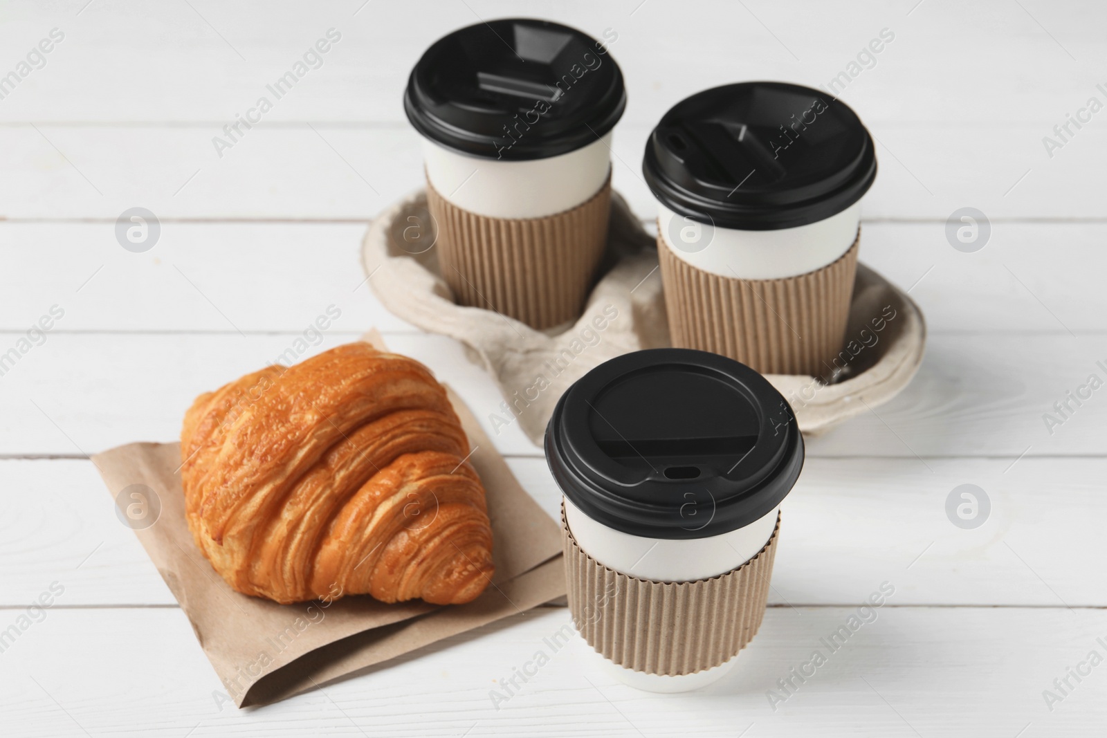 Photo of Coffee to go. Paper cups with tasty drink and croissant on white wooden table