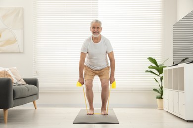 Senior man doing exercise with fitness elastic band on mat at home