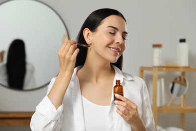 Photo of Young woman applying essential oil on neck indoors