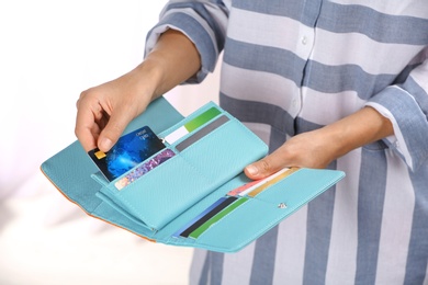 Photo of Woman taking out credit card from stylish wallet on light background, closeup