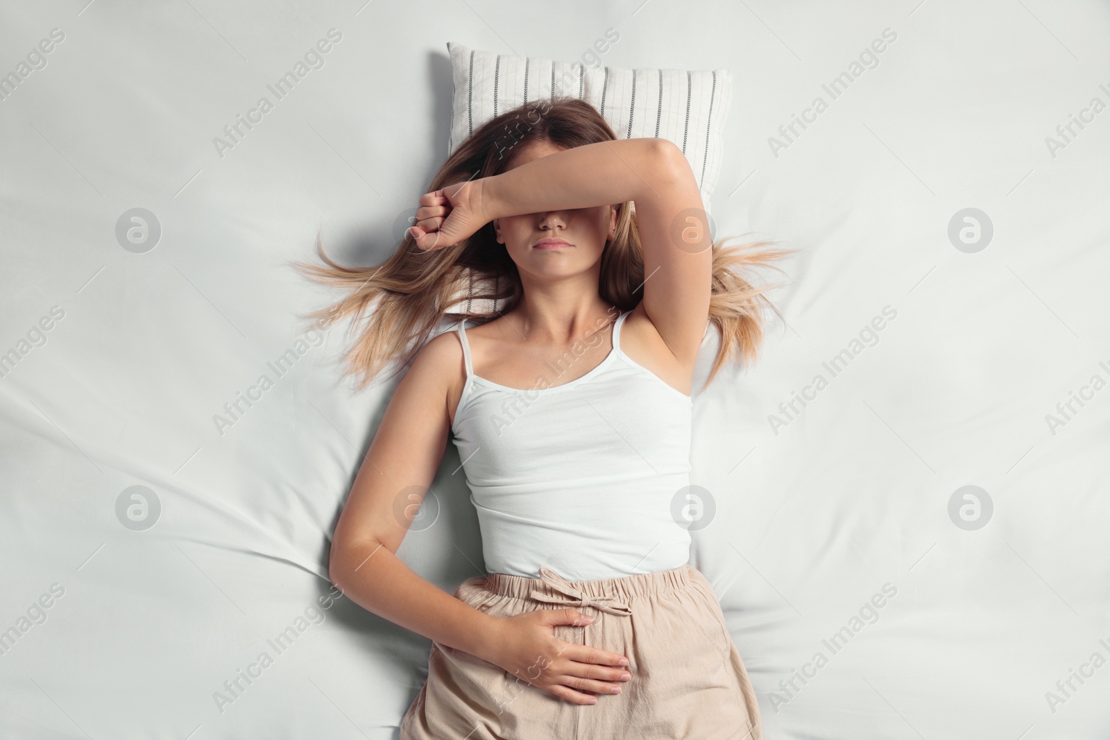 Photo of Young woman suffering from menstrual pain in bed, top view