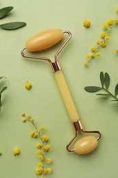 Photo of Natural face roller and flowers on green background, flat lay