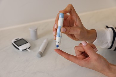 Photo of Diabetes. Woman using lancet pen at light table, closeup