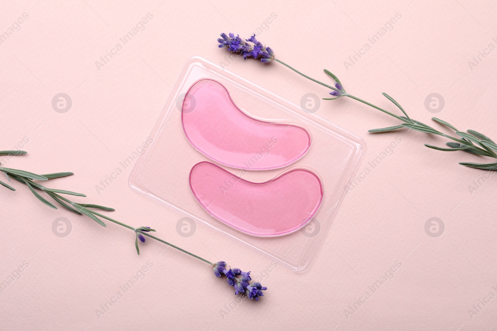 Photo of Package with under eye patches and lavender flowers on light pink background, flat lay. Cosmetic product