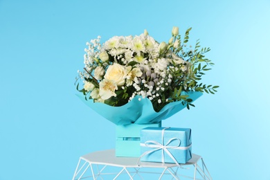 Photo of Beautiful bouquet of flowers and gift box on table against color background