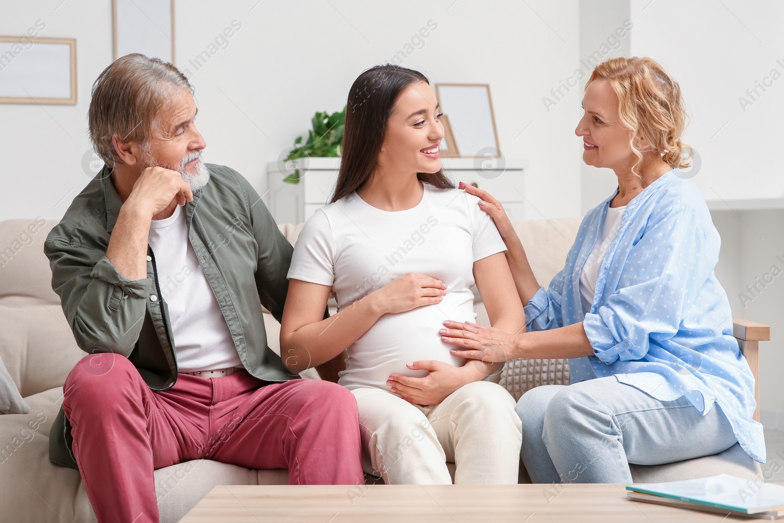 Photo of Happy pregnant woman spending time with her parents at home. Grandparents' reaction to future grandson