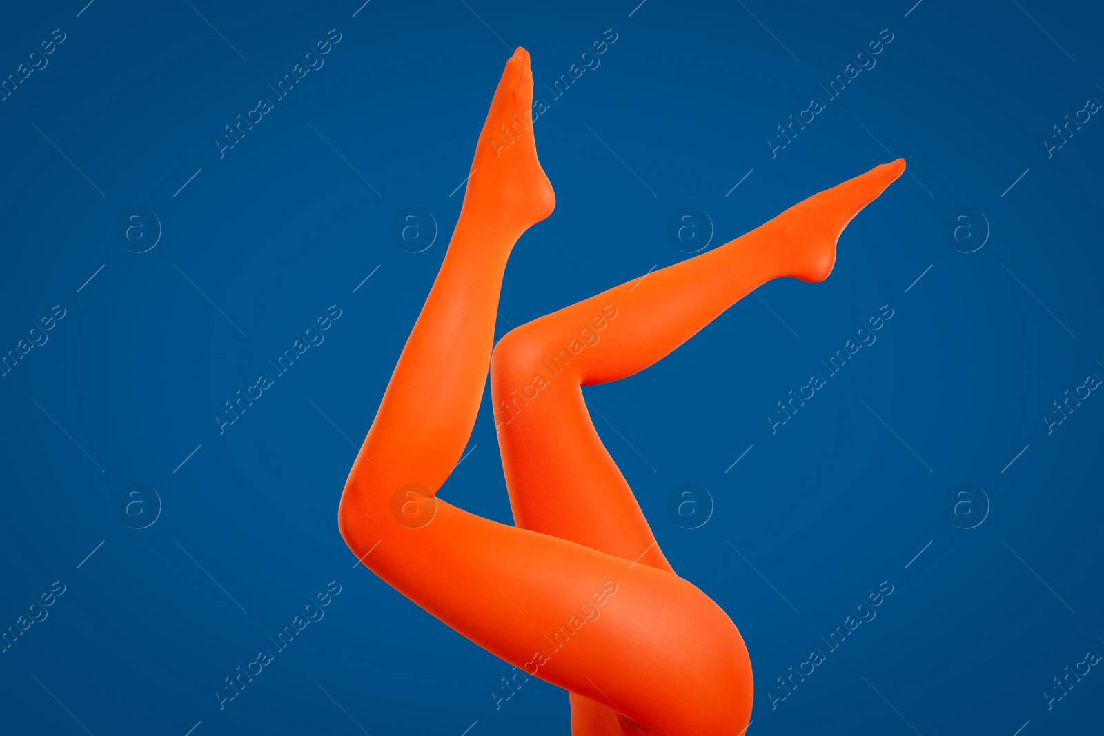 Photo of Woman wearing orange tights on blue background, closeup of legs