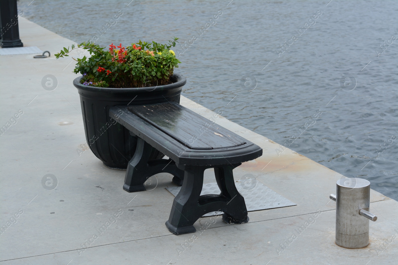 Photo of Stylish black bench and vase with beautiful plants on seashore