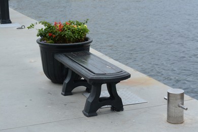 Stylish black bench and vase with beautiful plants on seashore