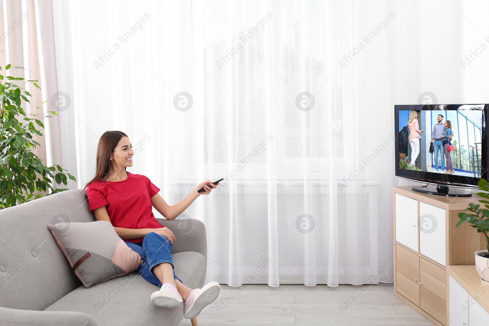 Photo of Beautiful young woman watching TV on sofa at home