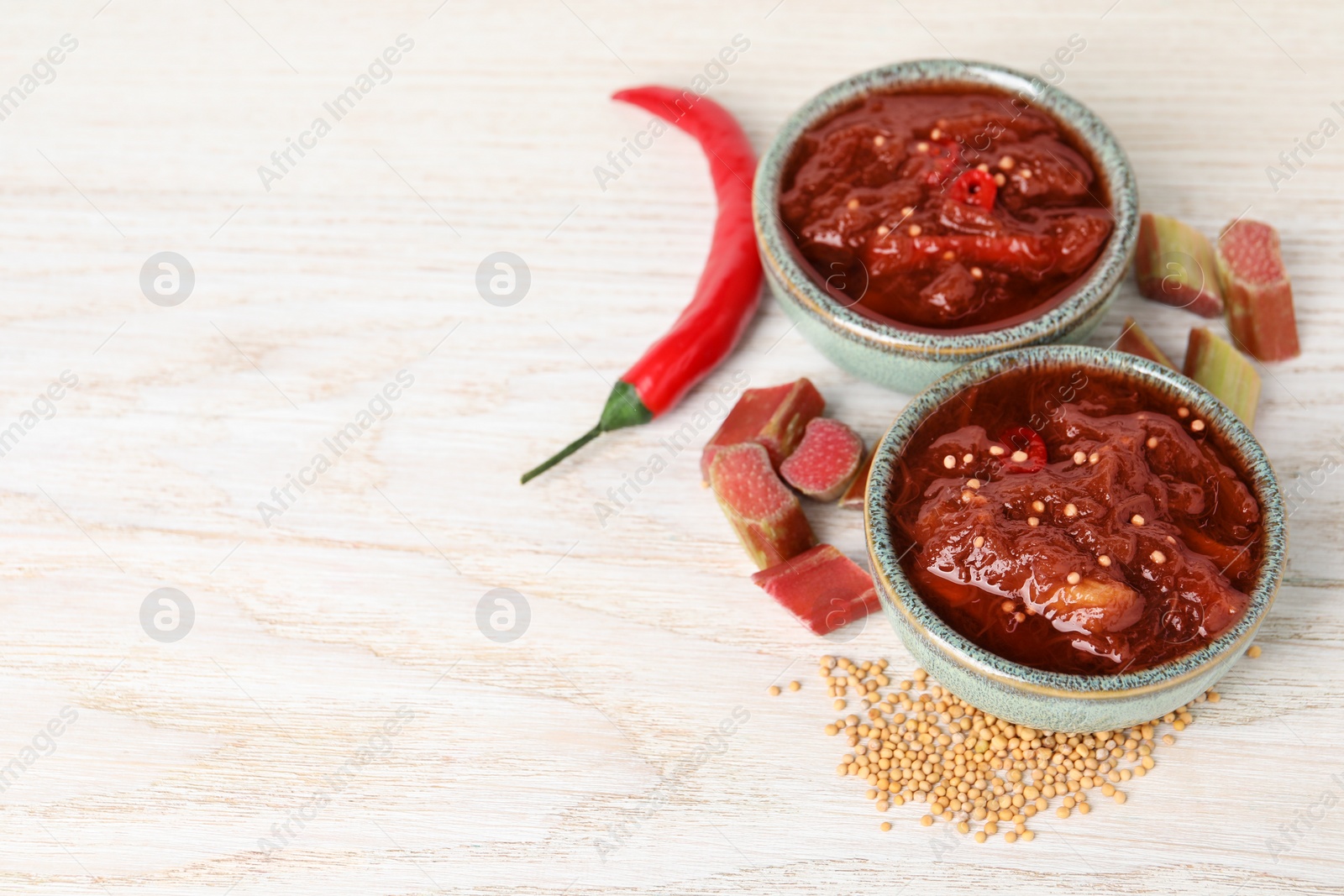 Photo of Tasty rhubarb sauce and ingredients on white wooden table, space for text