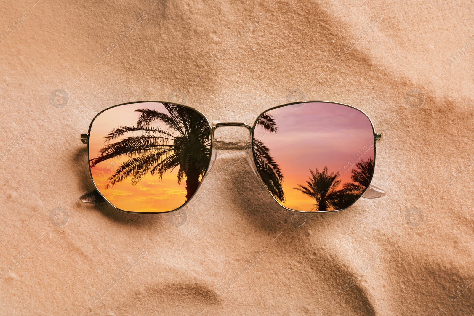 Image of Palms at beautiful sunset mirroring in sunglasses on sandy beach, top view