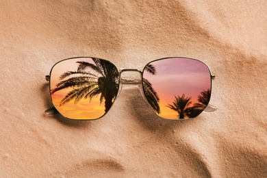 Palms at beautiful sunset mirroring in sunglasses on sandy beach, top view