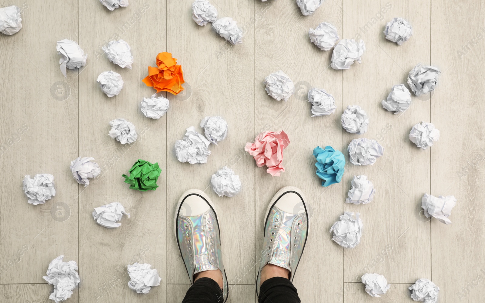 Photo of Closeup of person's feet surrounded by crumpled paper on floor, top view. Lack of ideas