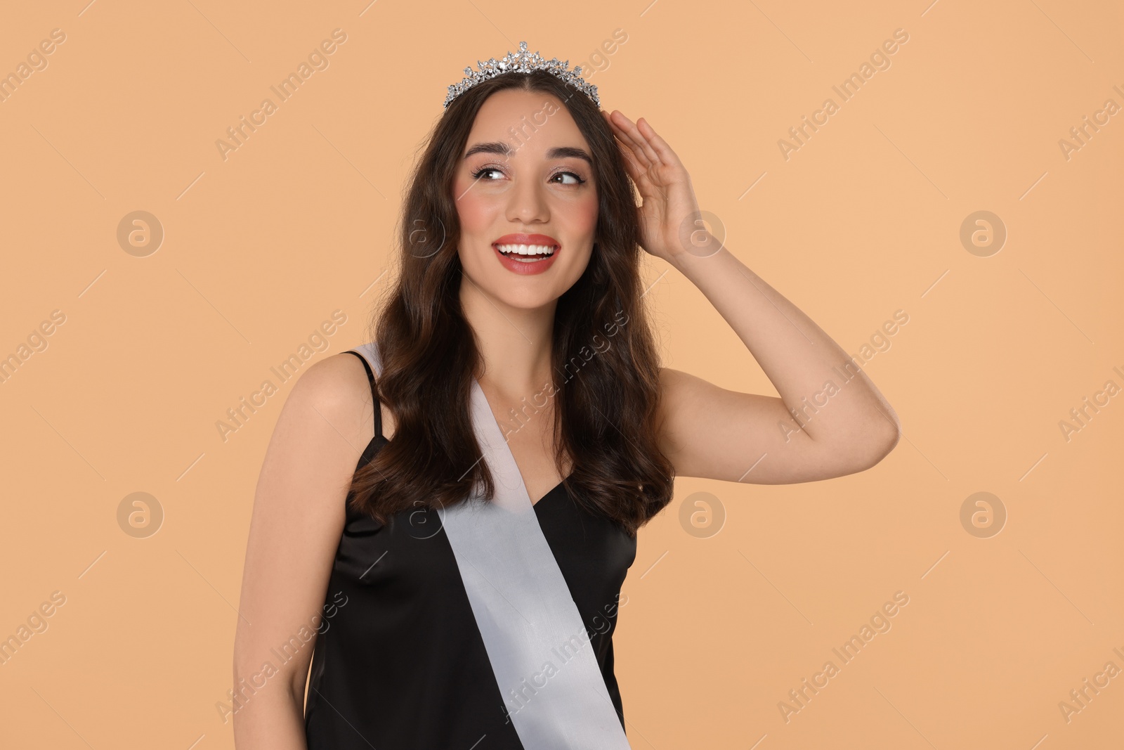 Photo of Beautiful young woman with tiara and ribbon in dress on beige background. Beauty contest