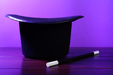 Black top hat and wand on wooden table. Magician equipment