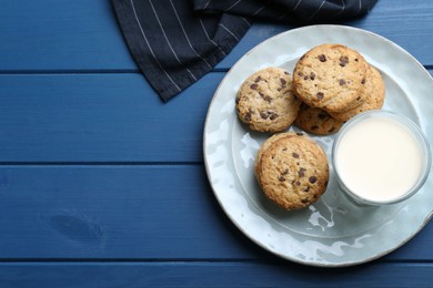 Photo of Tasty chocolate chip cookies and glass of milk on blue wooden table, flat lay. Space for text