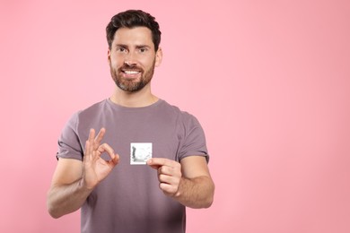 Man with condom showing ok gesture on pink background, space for text. Safe sex