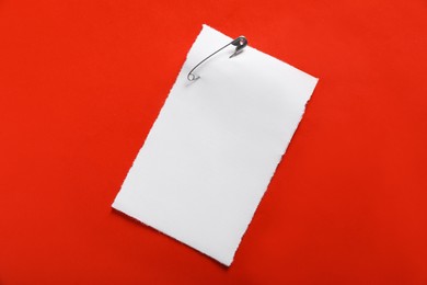 Photo of Sheet of paper attached with safety pin on red background, top view