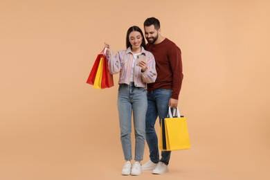 Happy couple with shopping bags and smartphone on beige background