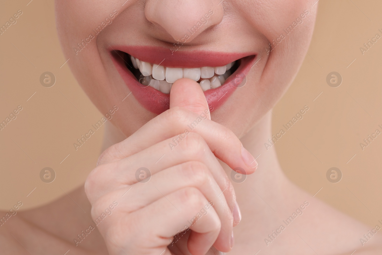 Photo of Young woman biting her finger on beige background, closeup